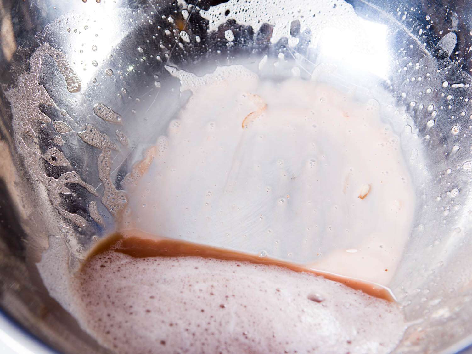 Brown water and hydrated potato starch at the bottom of a metal mixing bowl