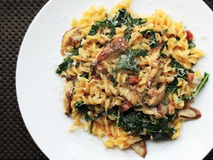Overhead shot of a plate of pasta tossed with pancetta, mushrooms, and wilted greens