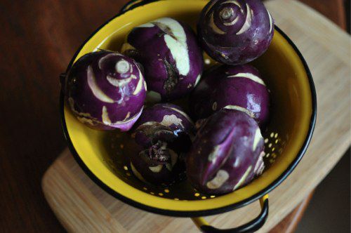 A yellow enamel colander full of trimmed and rinsed purple kohlrabi.