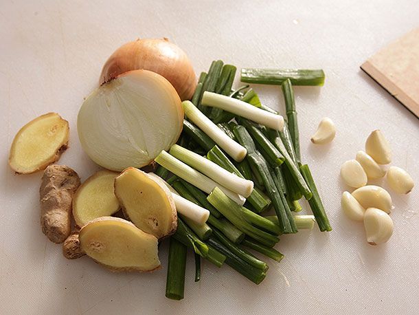 A pile of aromatics: fresh ginger slices, onion halves, scallion segments, and garlic.