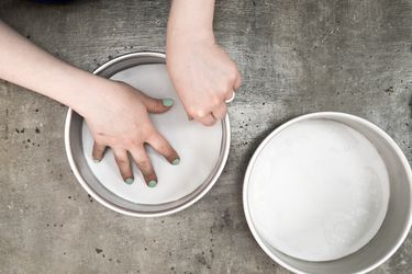 One round cake pan lined with a circle of parchment, hands pressing a circle of parchment into a second cake pan.