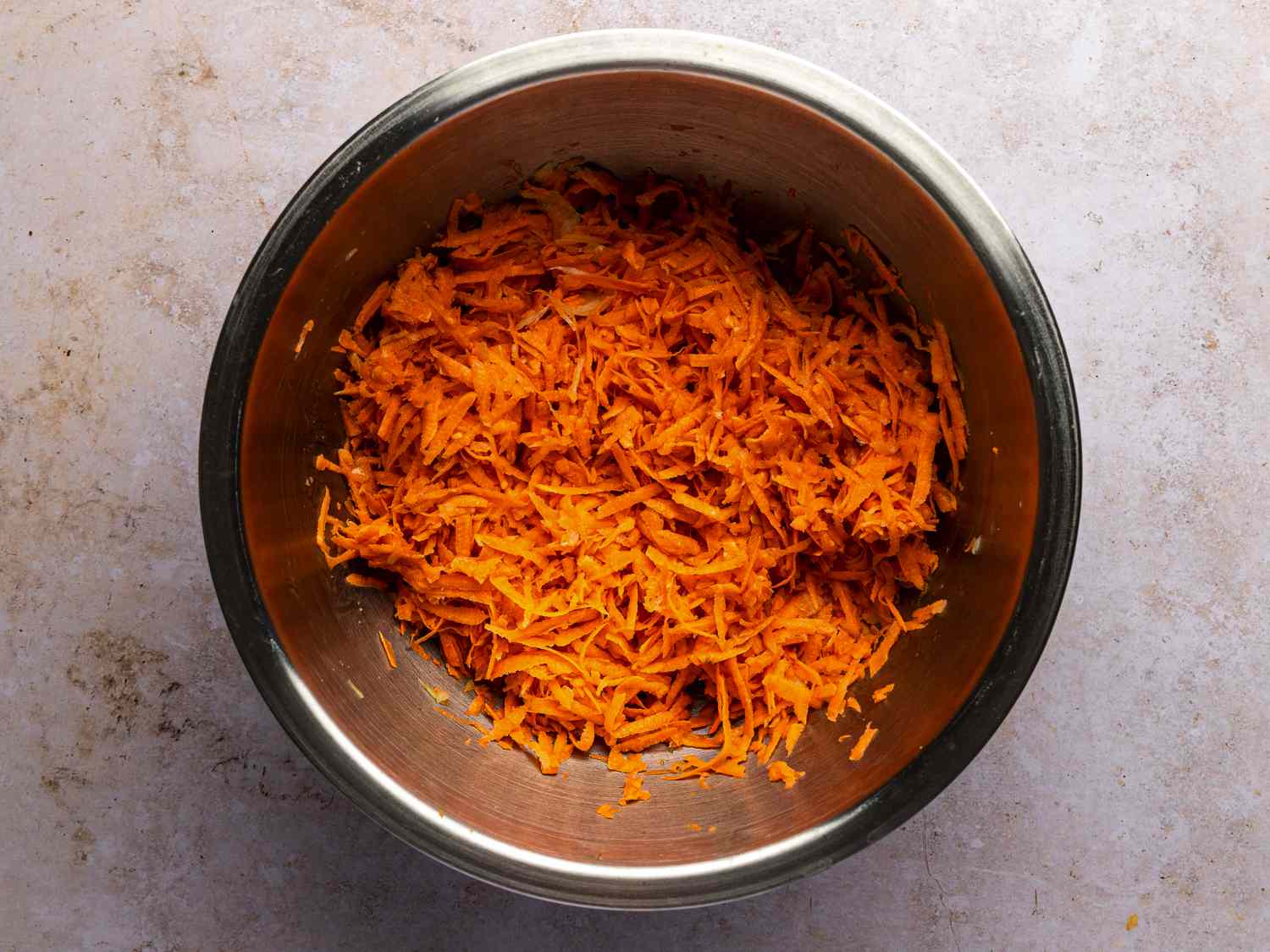 Grated onions and sweet potatoes in a metal bowl.