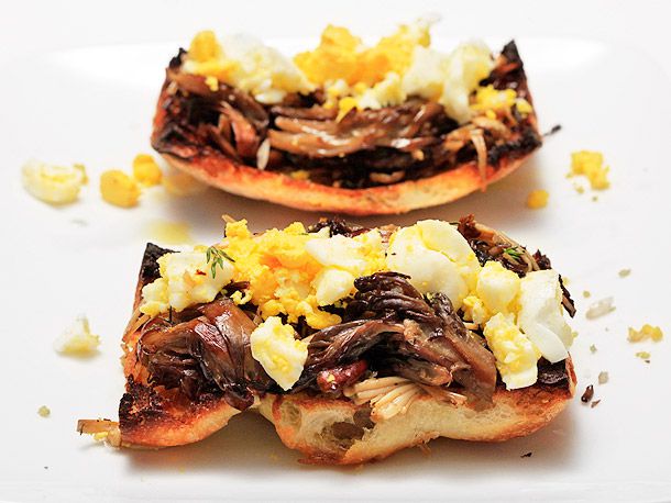 Two mushroom and crushed egg toasts, served as a tapa on a white plate.