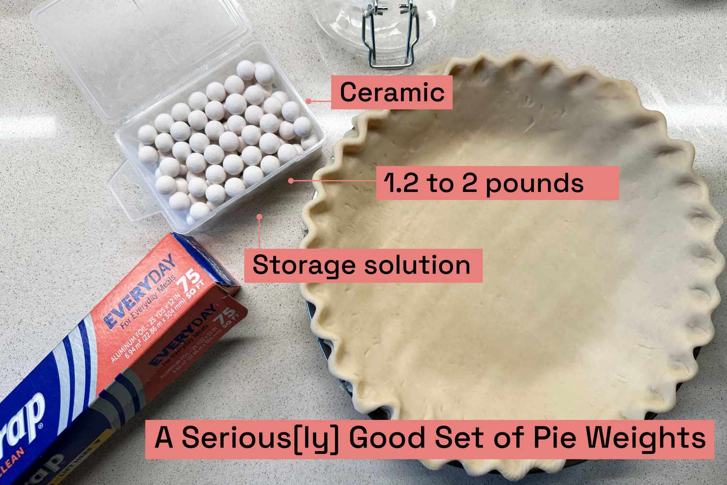 An unbaked pie shell next to a box of ceramic pie weights and a roll of aluminum foil.