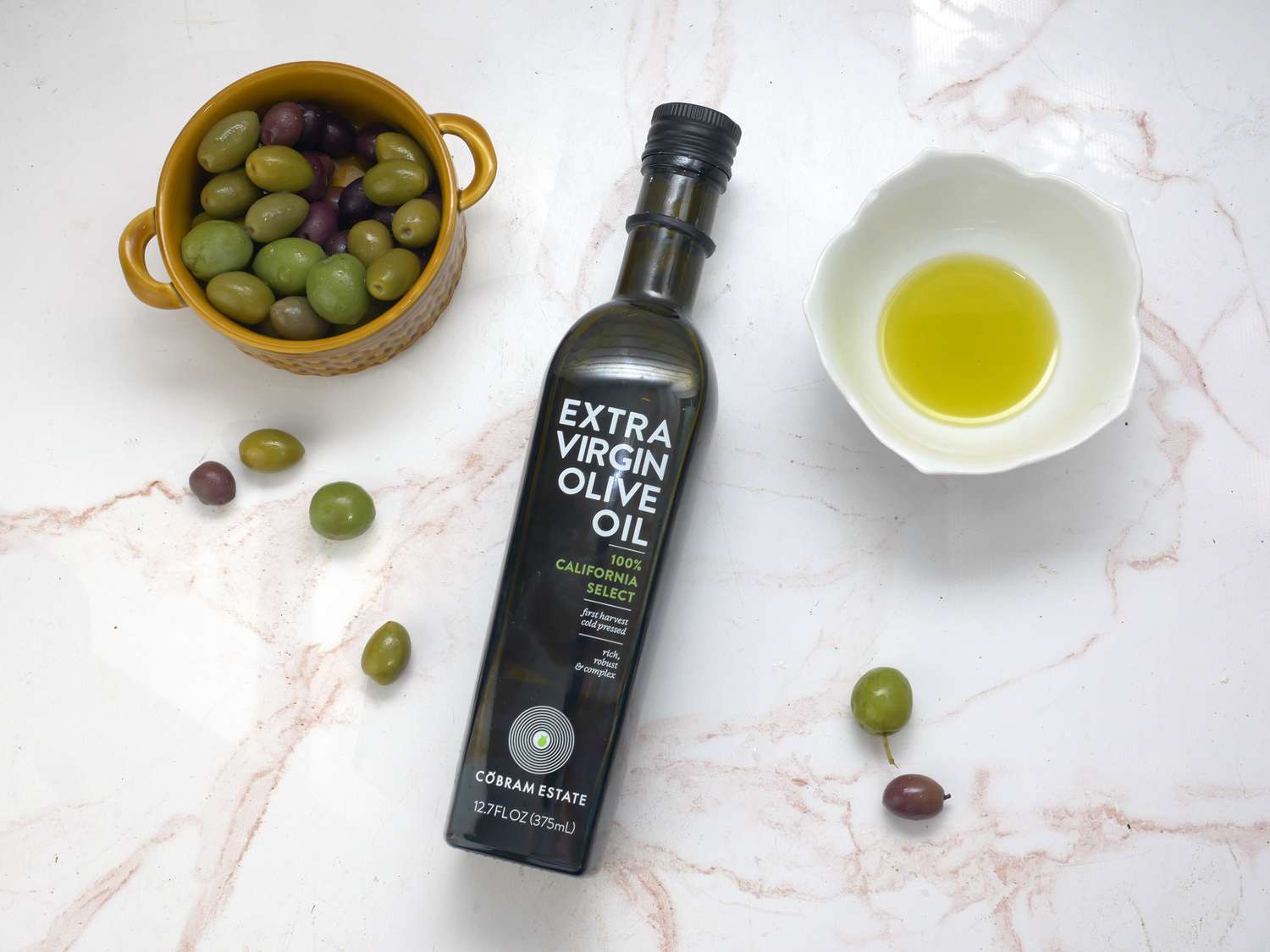 cobram olive oil bottle on a pink marble surface with olives and oil in a bowl