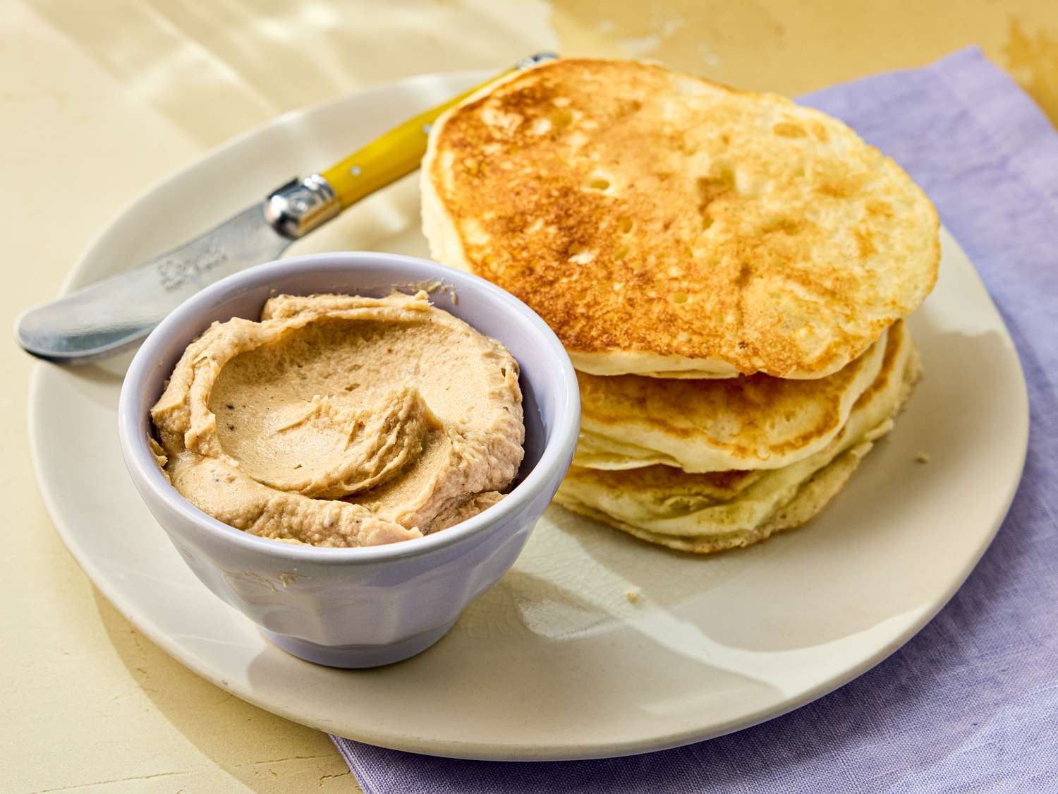 Plate with pancakes and a bowl of butter spread accompanied by a knife