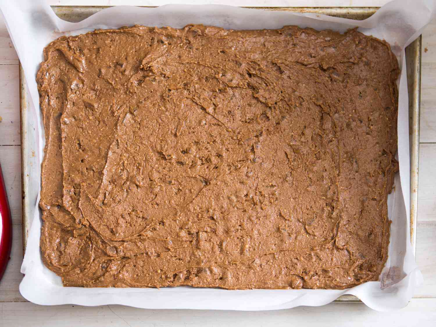 Lebkuchen dough spread out on a sheet of parchment paper inside of a baking pan.
