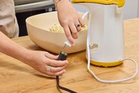 A person plugs the Presto Poplite Hot Air Popper into a power cord