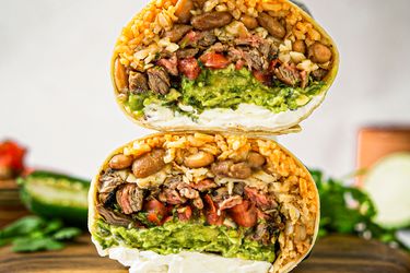 A stacked burrito crosssection showing fillings such as meat beans rice guacamole and cream cheese on a wooden surface