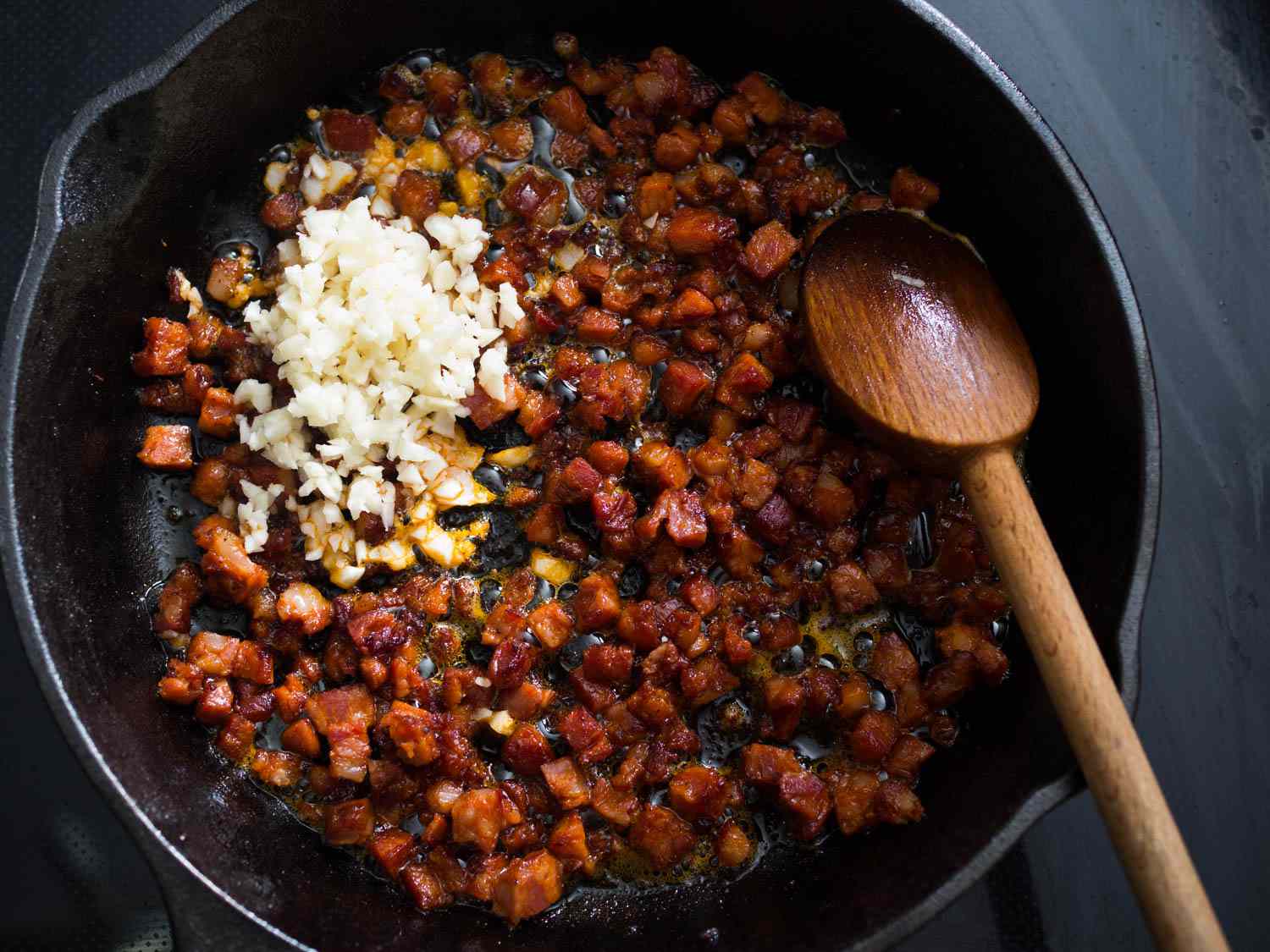 Overhead view of browned, crispy diced chorizo in a cast iron skillet. Minced garlic has just been added.
