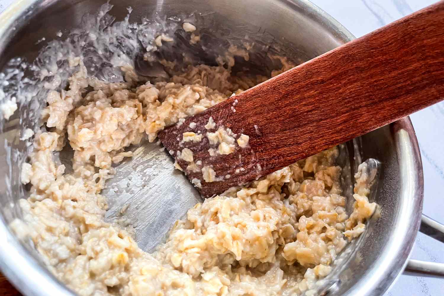 A pot with oatmeal being stirred by a wooden spoon