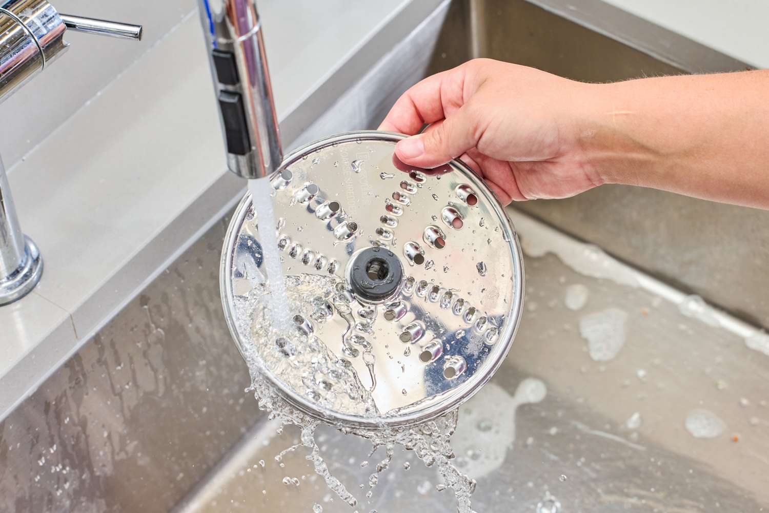 A person washes a blade from the Breville BFP660SIL Sous Chef 12-Cup Food Processor