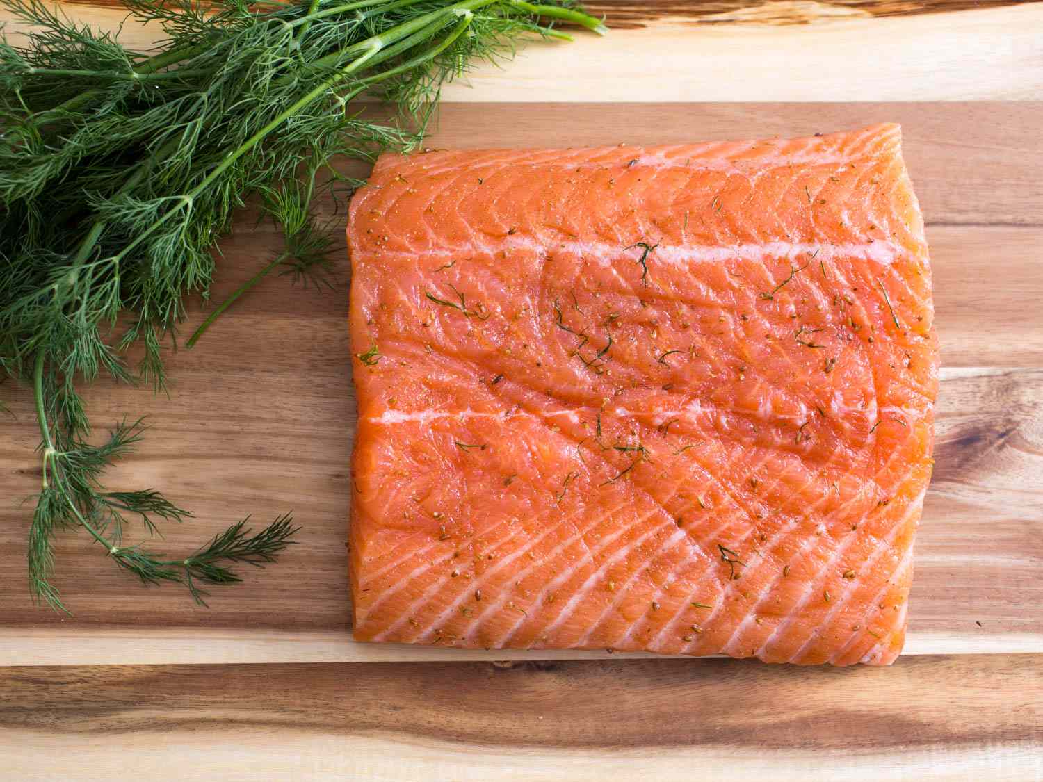 Finished gravlax with fresh dill on a wooden cutting board. 