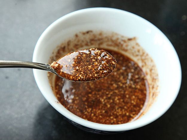 A spoonful of burnt galric-sesame-chile oil is held up to the camera. A bowl of the condiment is visible below.