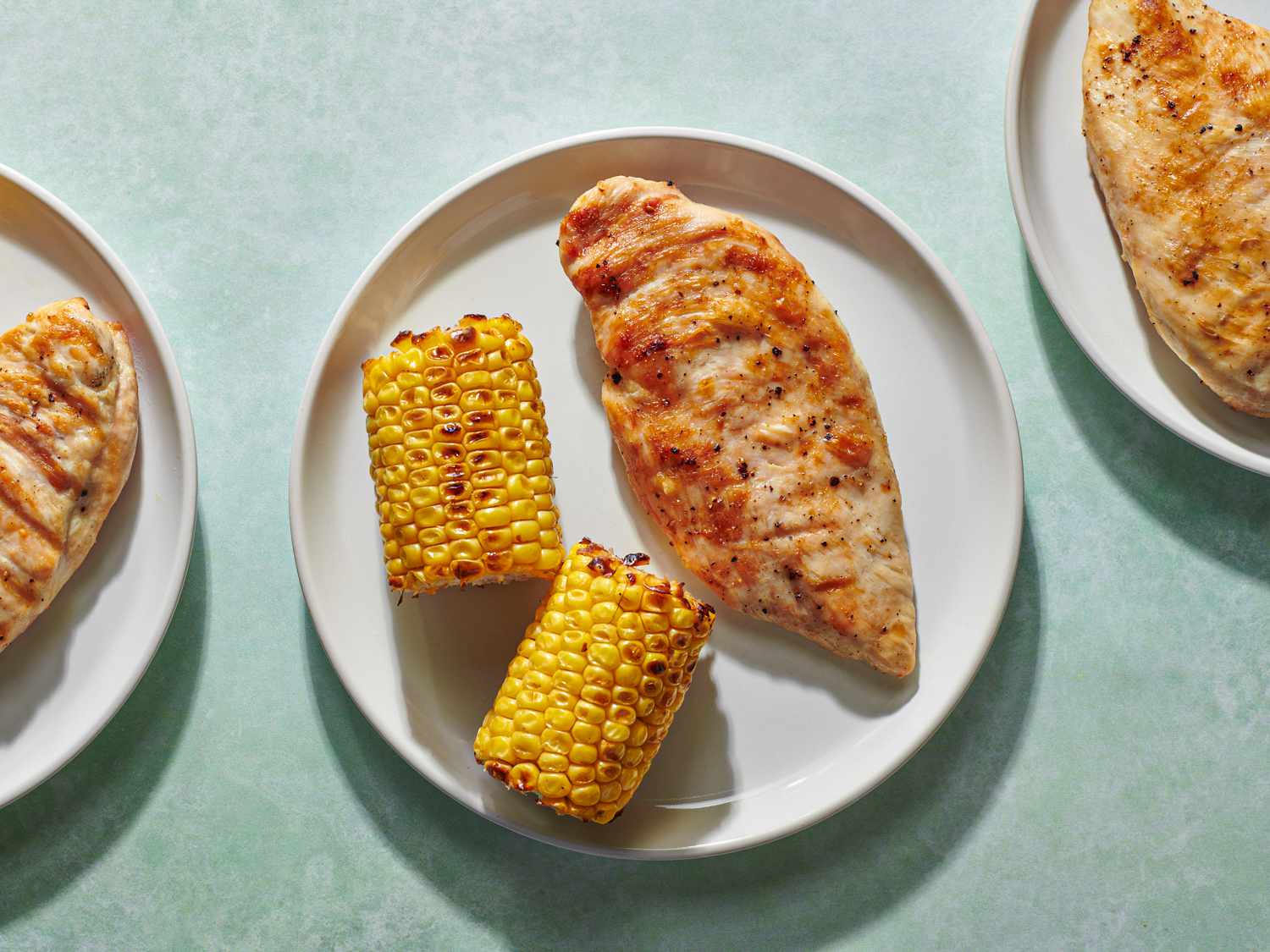 A grilled boneless chicken breast on a white ceramic plate along with two grilled pieces of corn-on-the-cob.