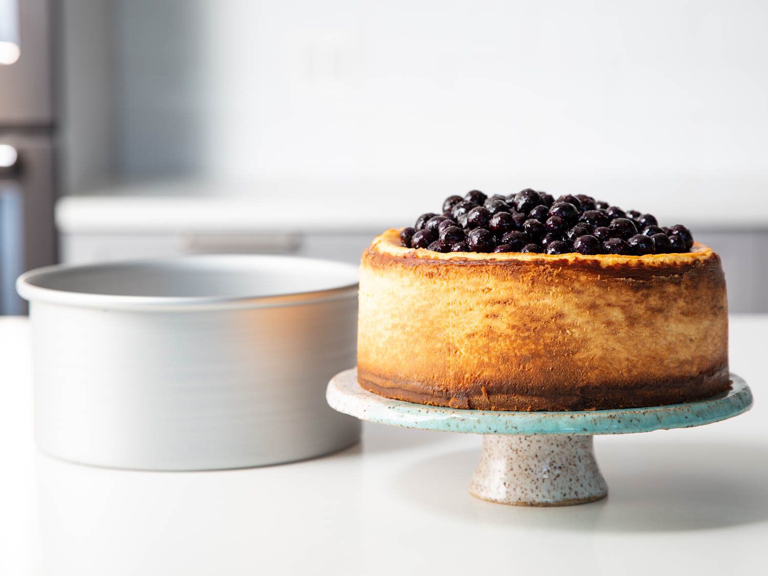 a New York style cheesecake on a pedestal, topped with blueberries