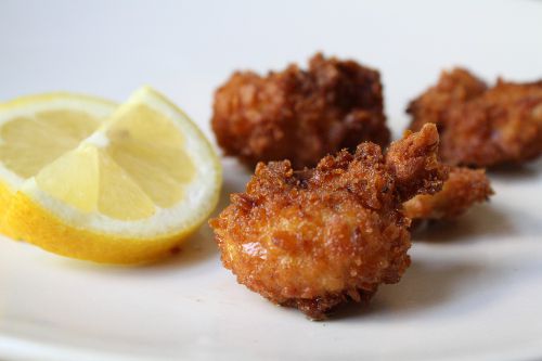 Closeup of deep-fried testicles served on a white plate with lemon wedges.