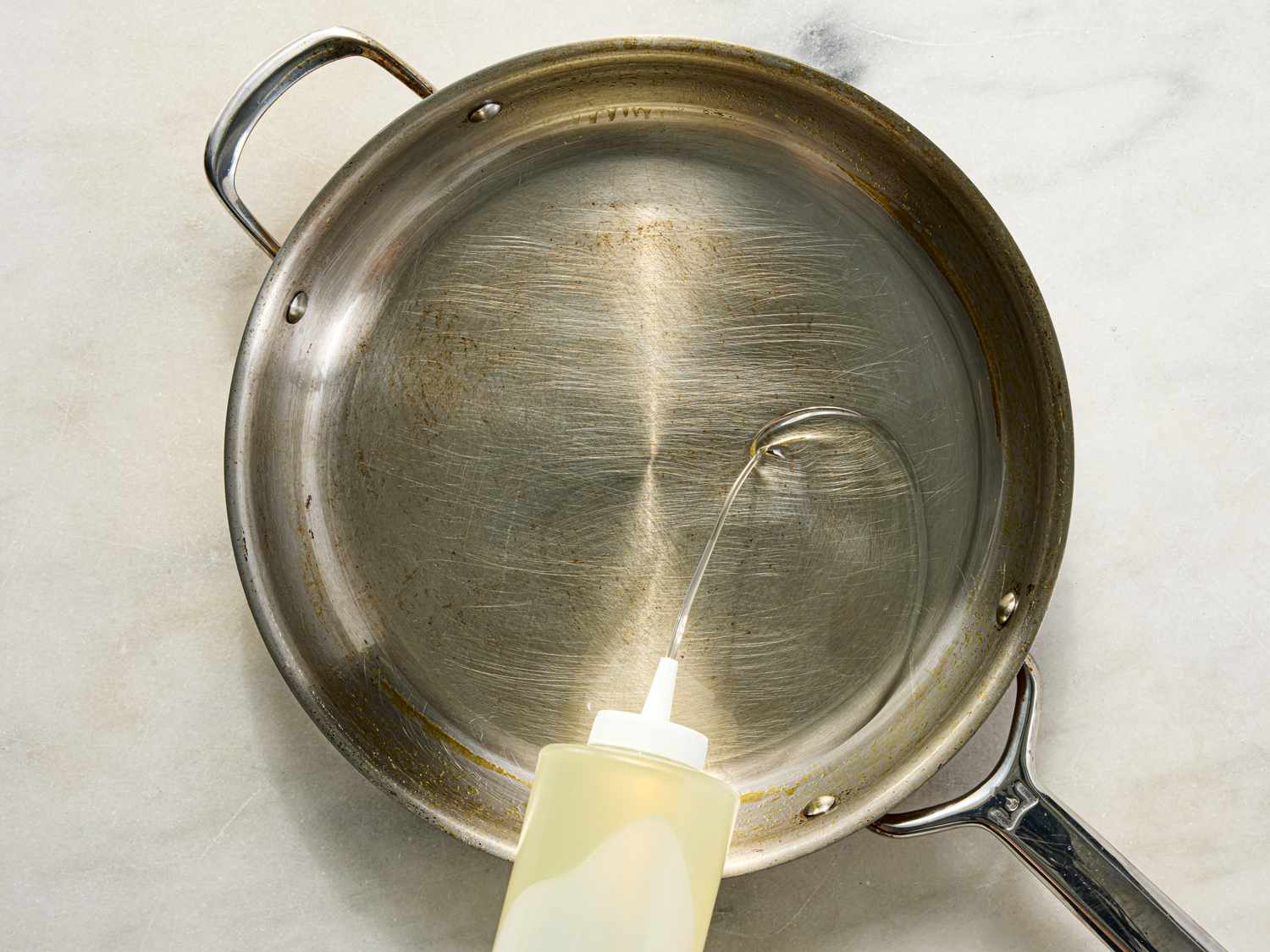 A frying pan on a countertop with oil being poured into it from a squeeze bottle