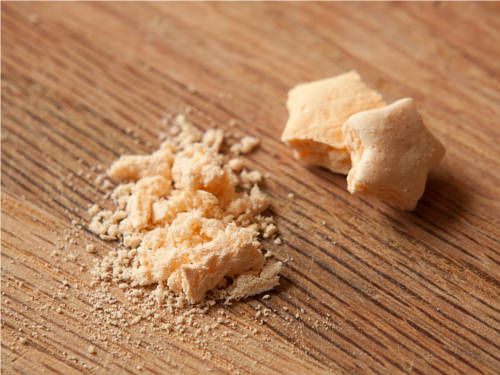 A pile of crispy cereal marshmallows. Nearby, one of them has been crushed into dust.