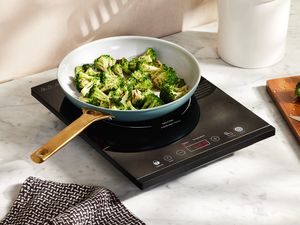 A ceramic pan filled with broccoli atop an induction burner.