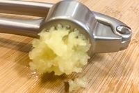A garlic press with minced garlic on a wooden surface