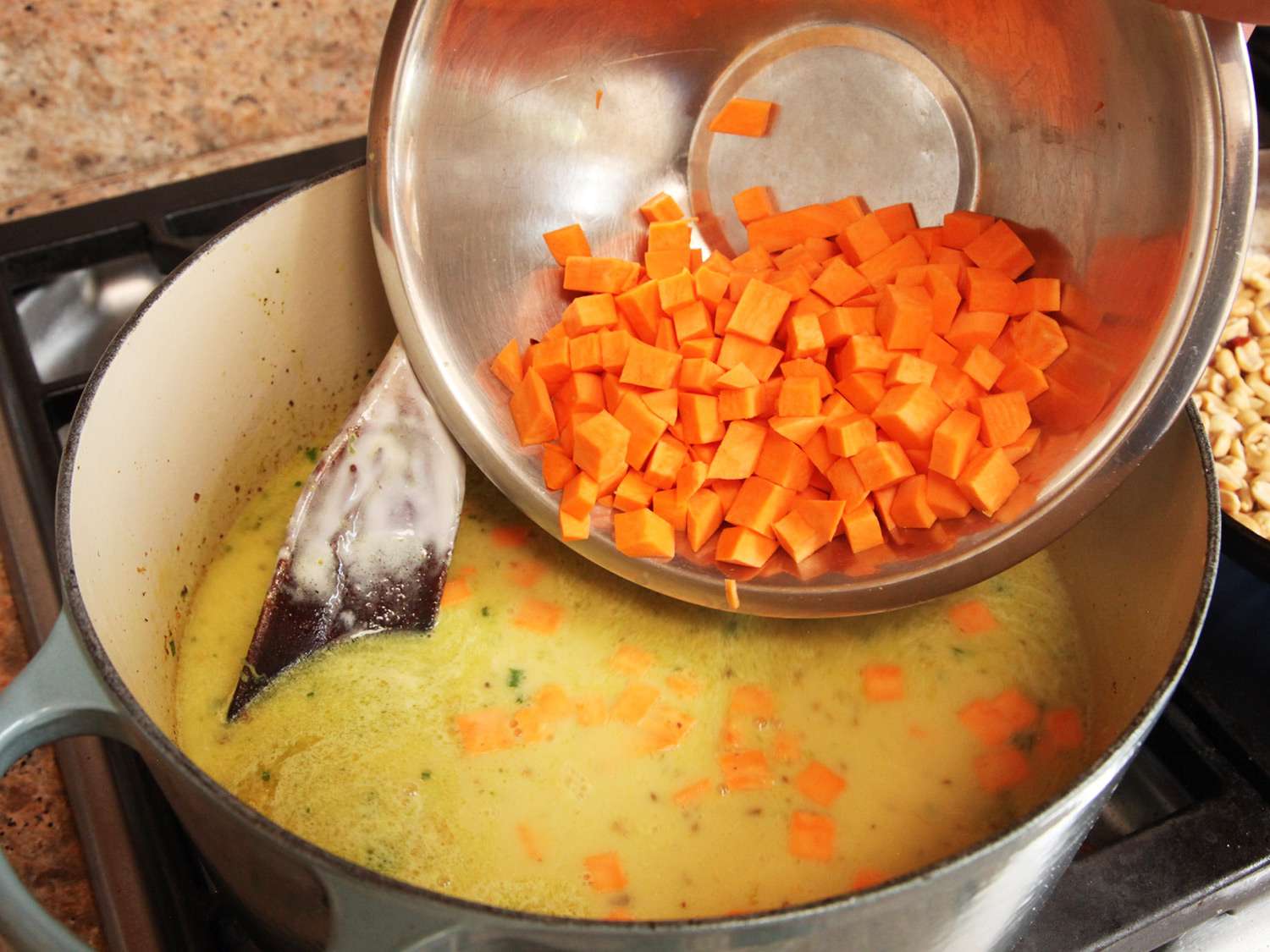 Adding cubed sweet potatoes to a pot of peanut soup.