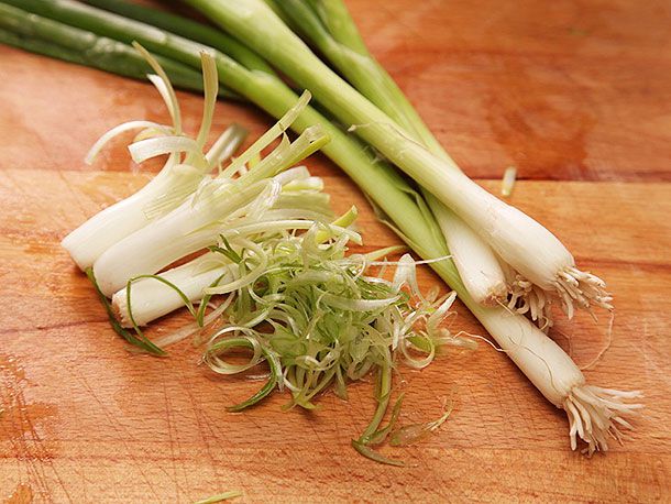 Scallions which are whole, slivered, and sliced on a cutting board.