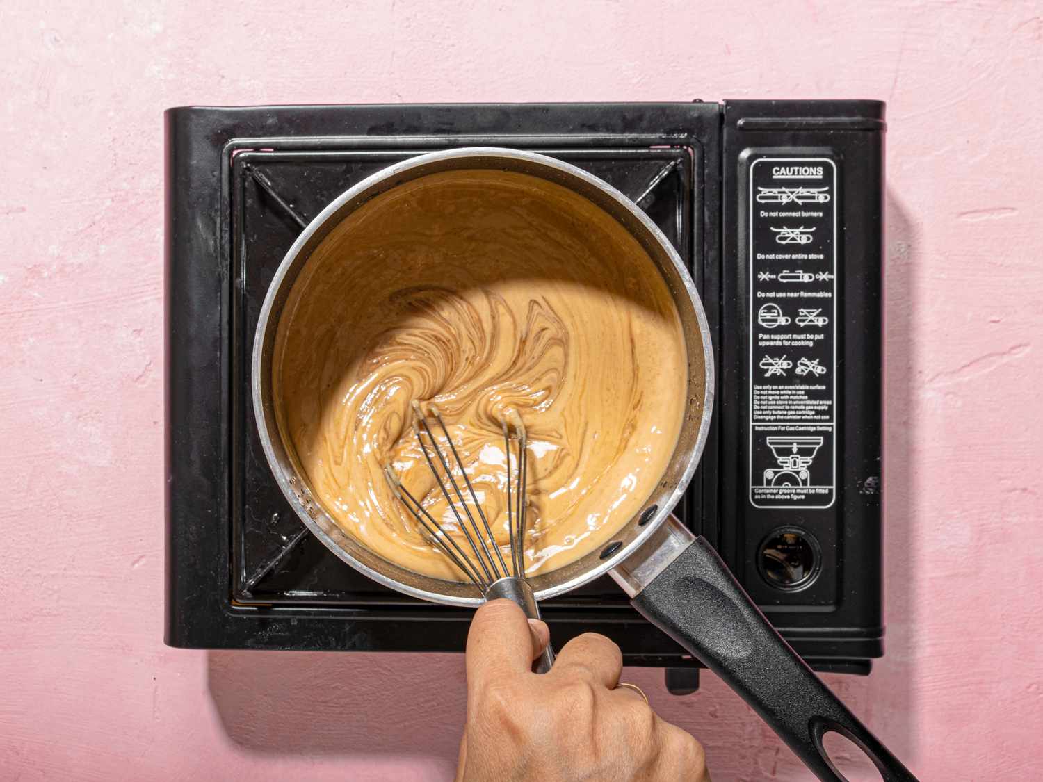 Hand whisking mixture in a saucepan on a stovetop