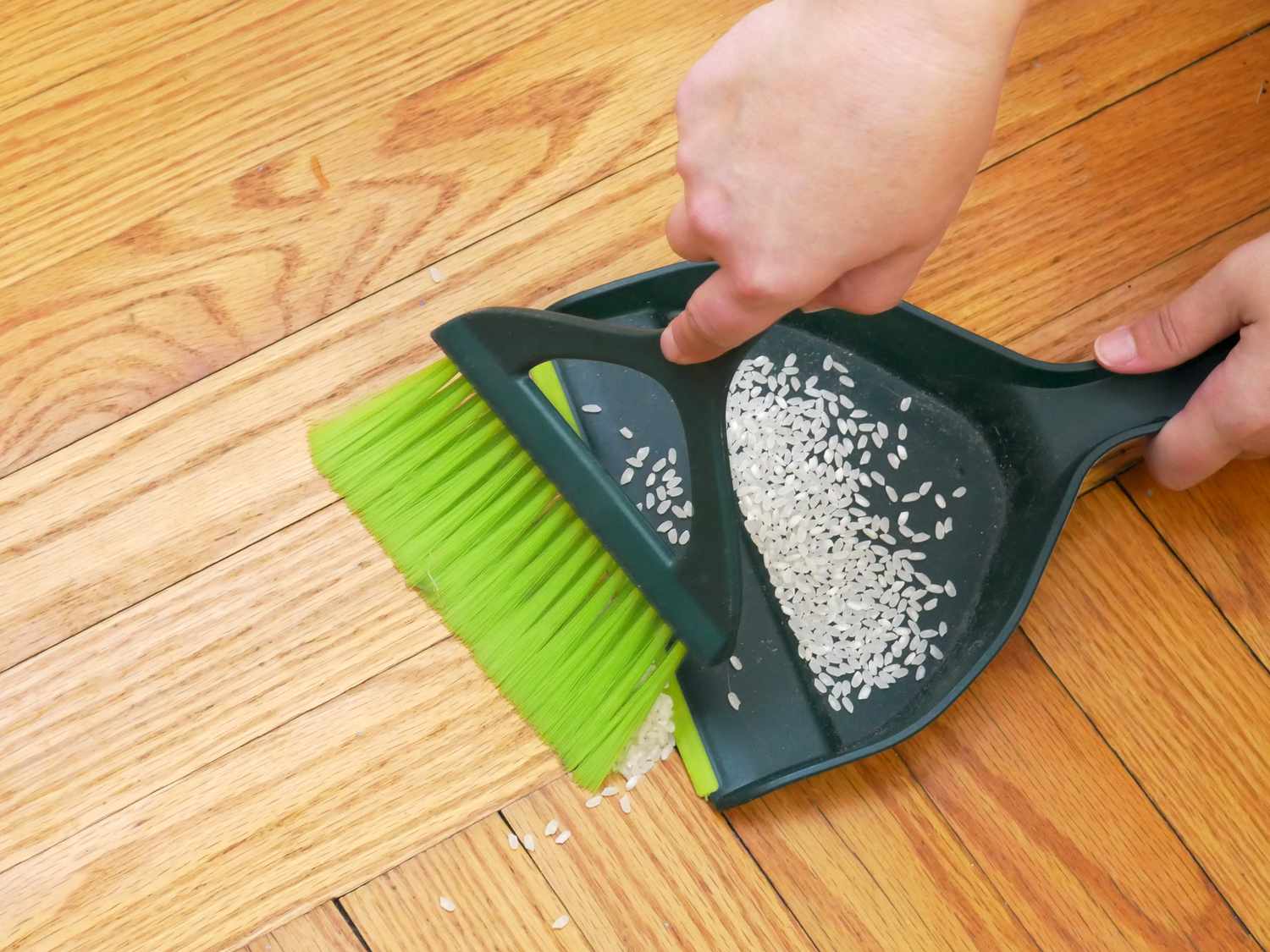 a person using the pin sol dustpan and brush to sweep up rice
