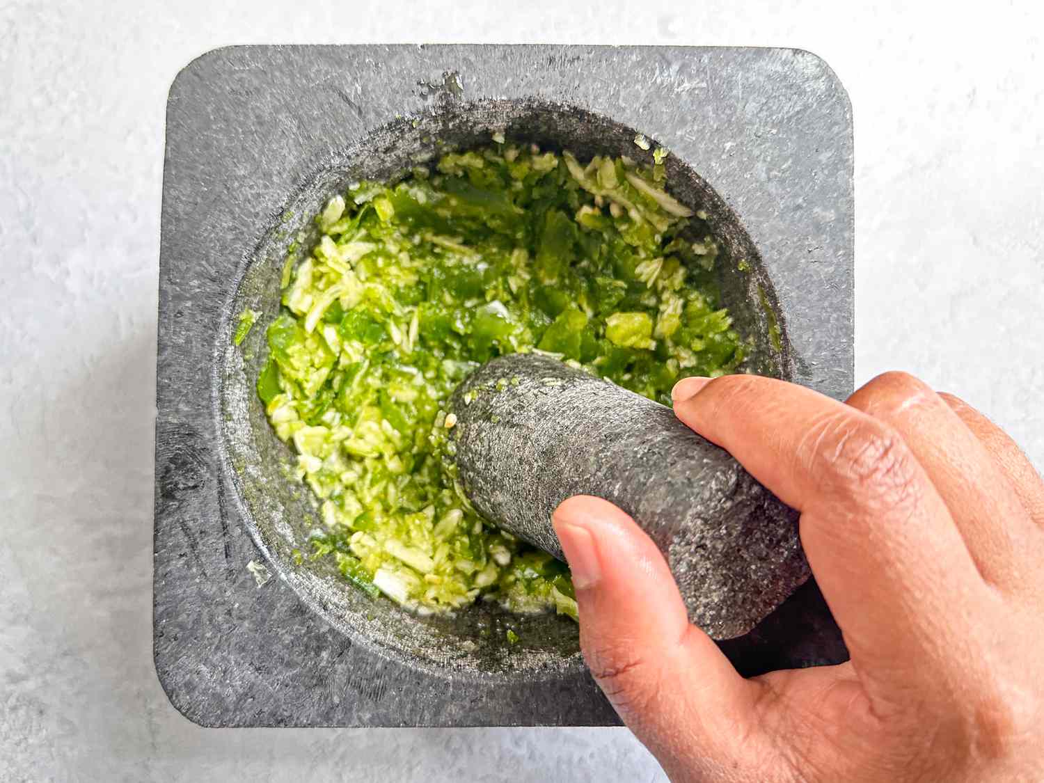 A hand using a mortar and pestle to grind green herbs and garlic