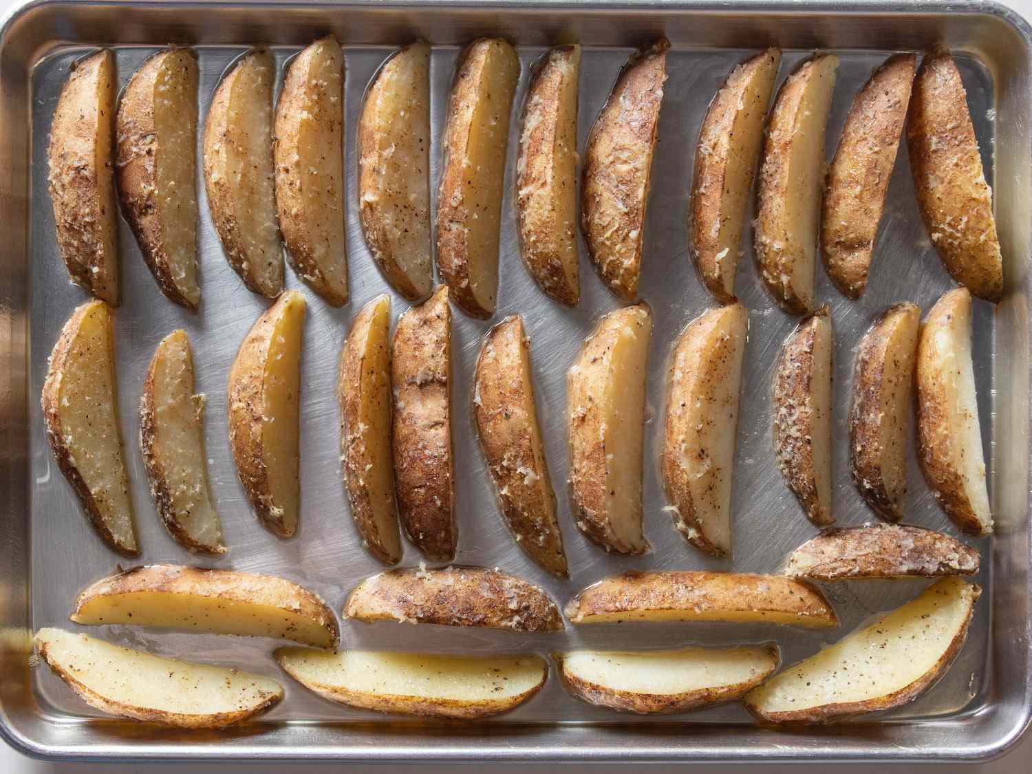 Potato wedges arranged on an oiled baking sheet before going in the oven.