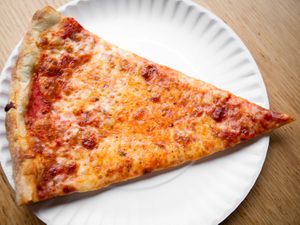 A slice of New York style cheese pizza on a white paper plate. 