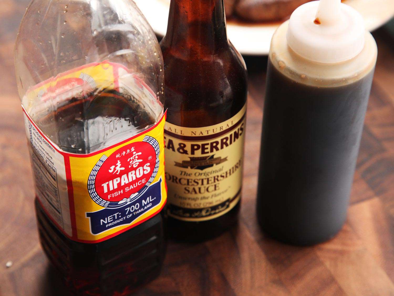 Bottles of fish sauce, Worcestershire sauce, and soy sauce resting on a cutting board.