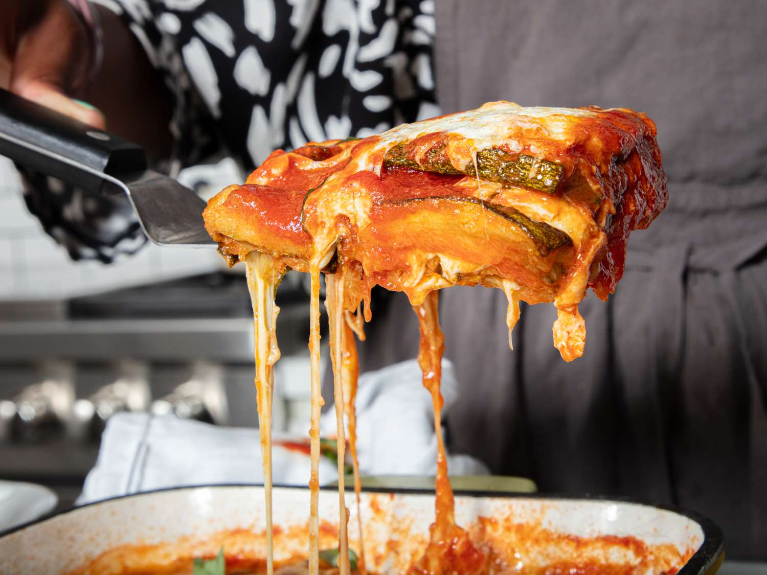 A portion of zucchini parmesan being lifted with a spatula showcasing cheese and sauce
