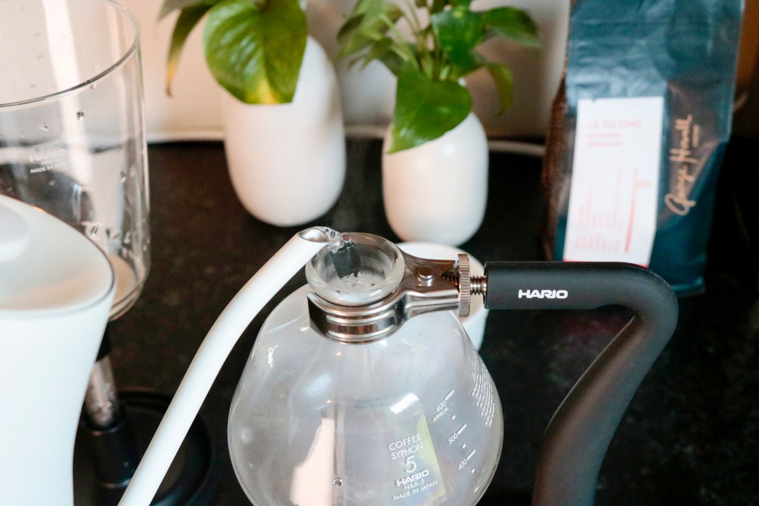 a gooseneck kettle pouring water into the bottom chamber of a coffee siphon