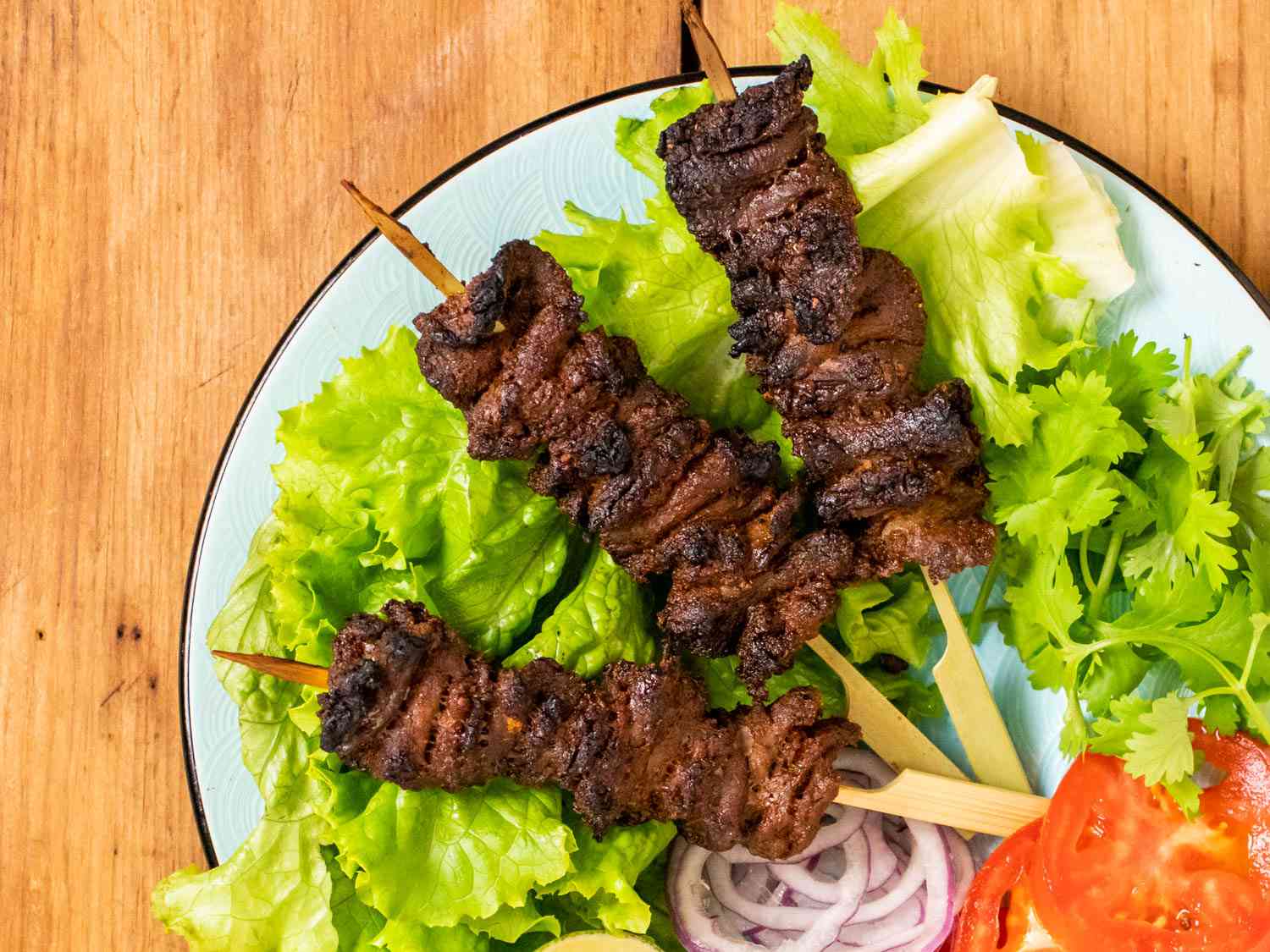 Spiced Nigerian beef skewers plated on a lettuce leaves with sliced red onion and tomato