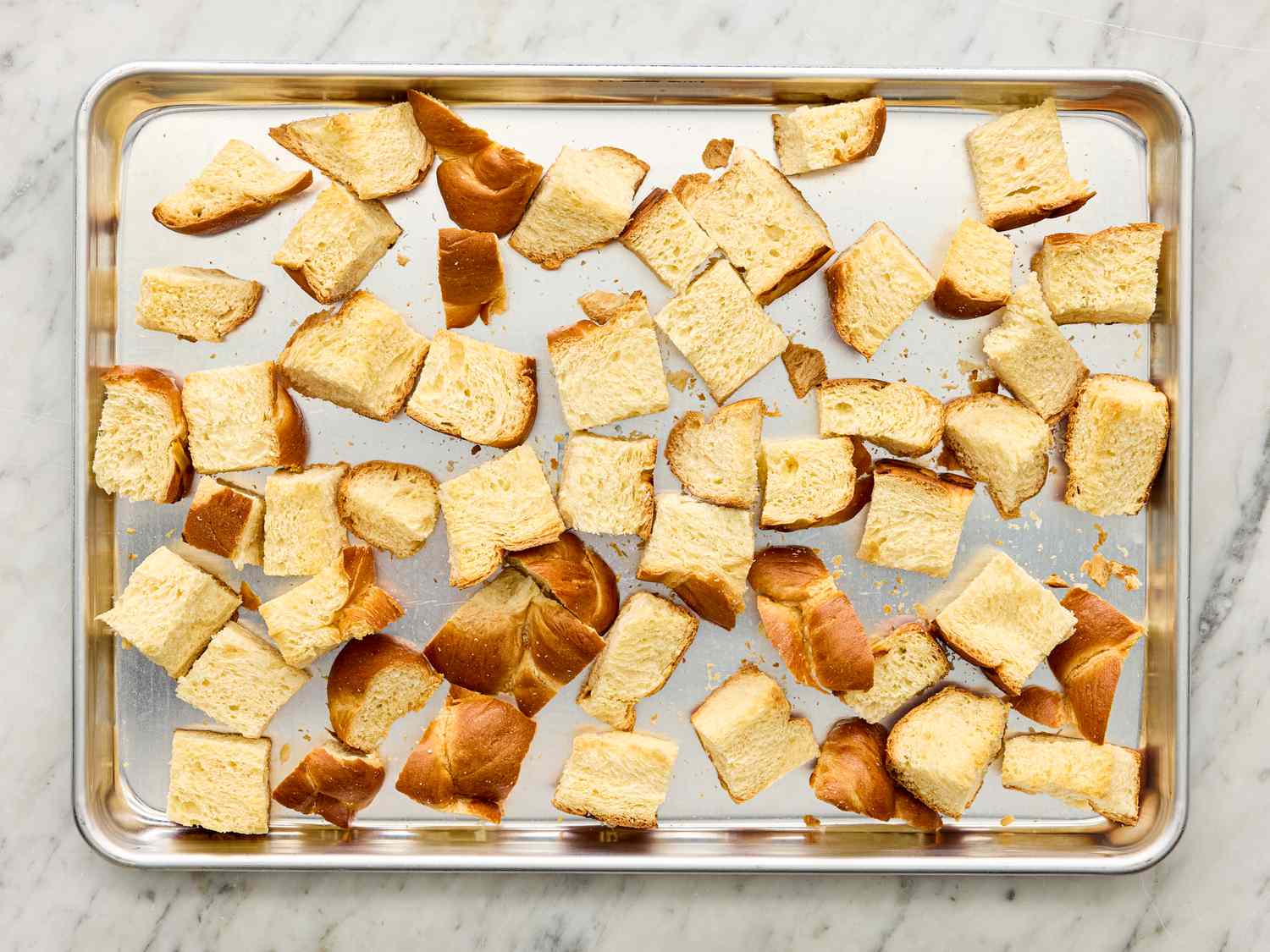 Chunks of bread spread on a baking sheet preparation for bread pudding