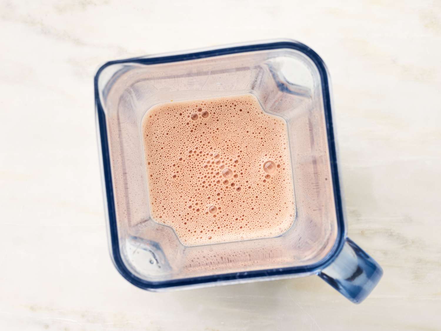 A blender with vinaigrette inside, resting on a light-colored surface