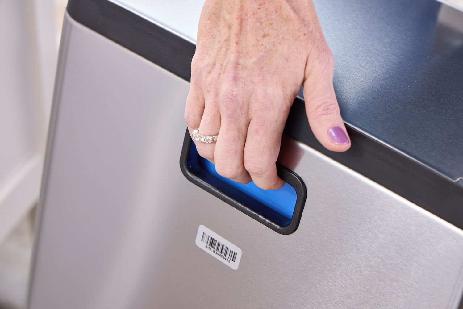 A person lifts the simplehuman 38-Liter Brushed Stainless Steel Steel Trash Can with Lid by the handles