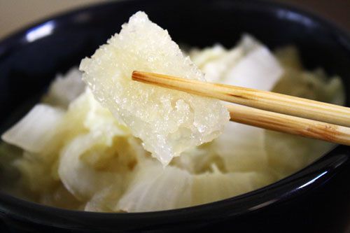 Closeup of a cooked piece of chicharron held up to the camera with a pair of chopsticks.
