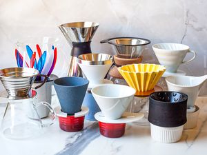 Various pour-over coffee drippers arranged on a marble surface, showcasing different designs and materials