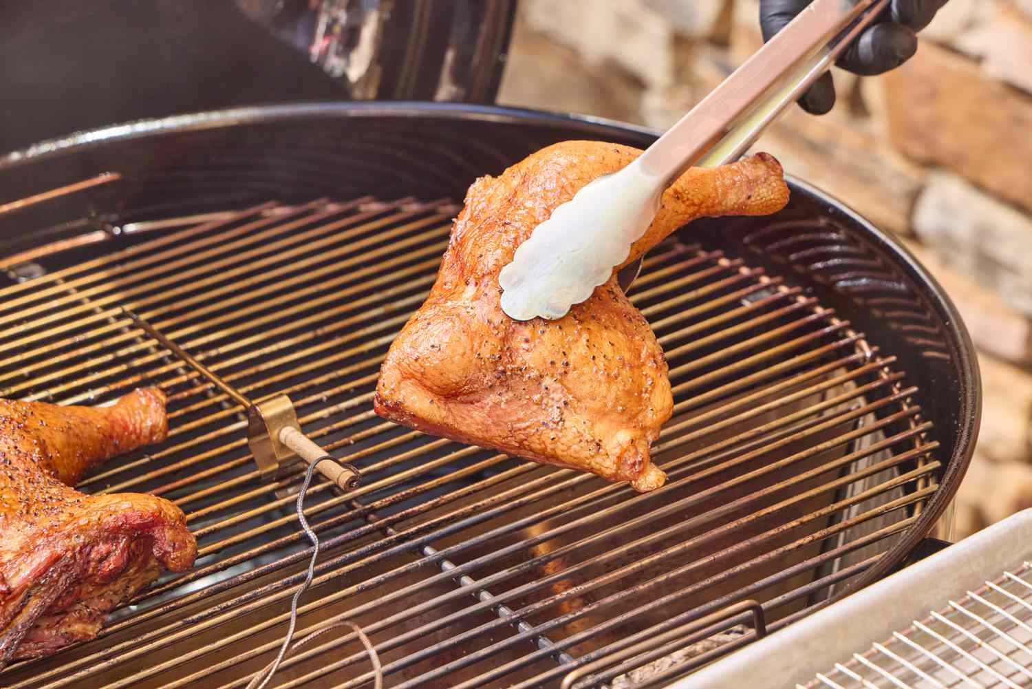 A hand using tongs to lift chicken in the SNS Grills Slow 'N Sear Original 22-Inch Kettle Grill