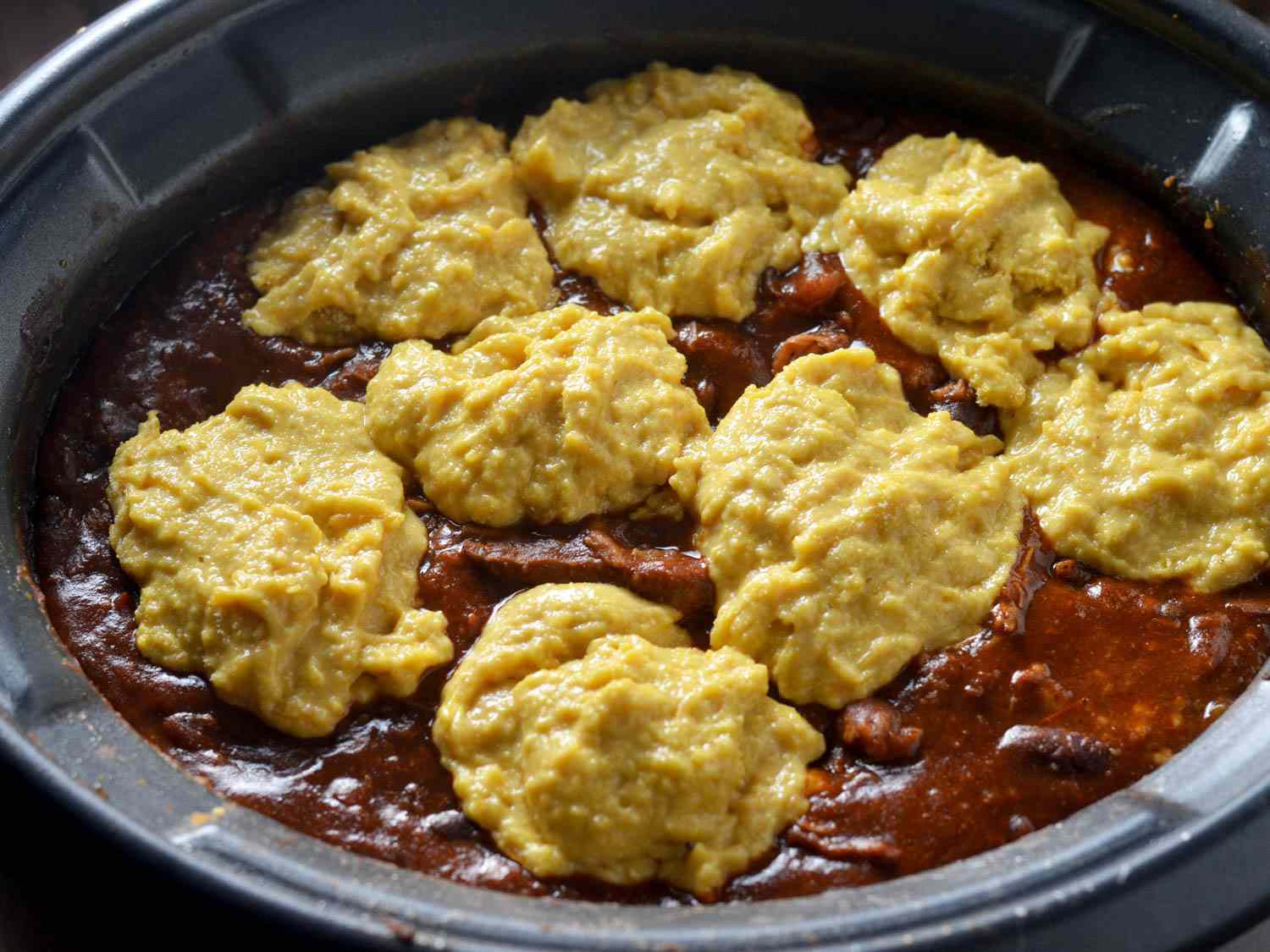 Raw cornbread batter in dollops on top of chili in a slow cooker
