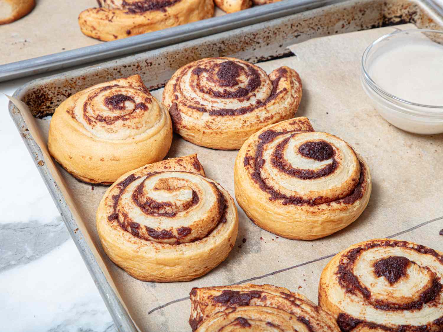 Tray of baked cinnamon rolls with a bowl of glaze nearby