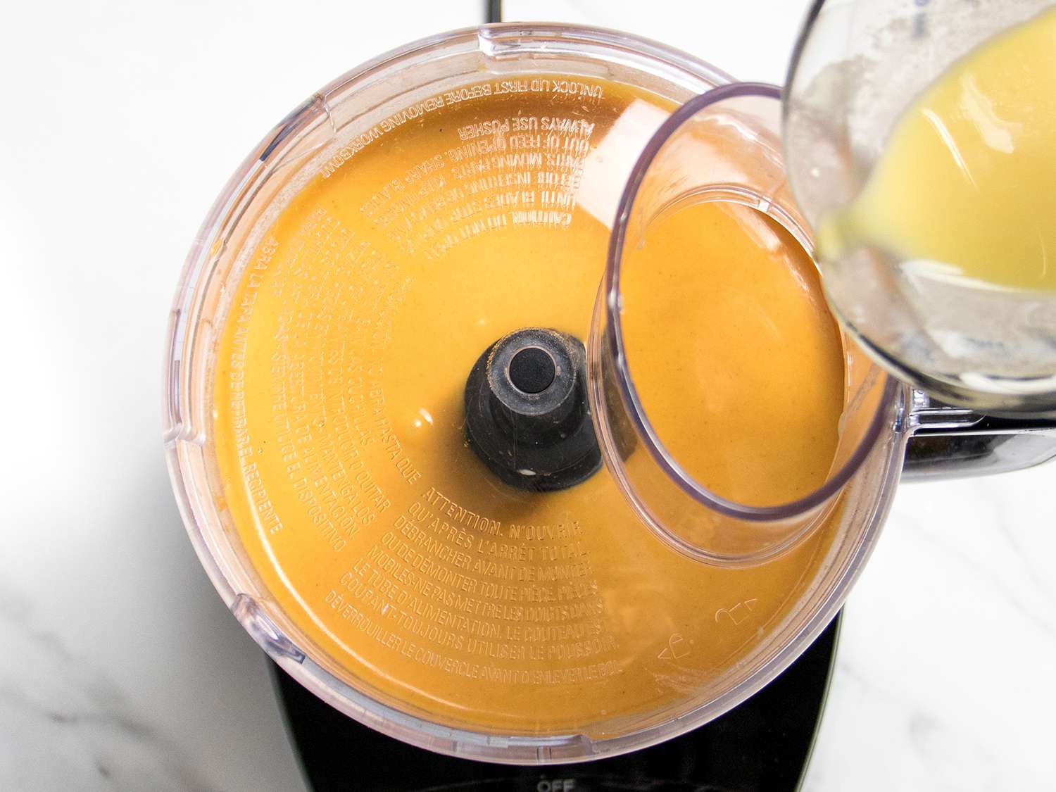 Egg mixture being poured into cheesecake base in the food processor.