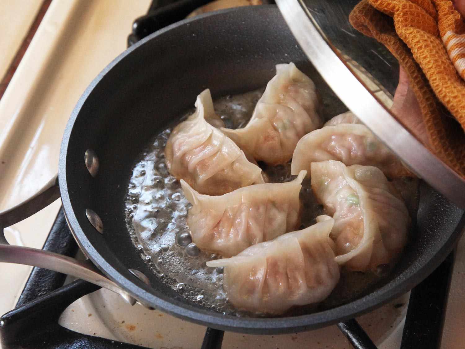 Lifting the lid off a pan of steamed pork and cabbage gyoza. 