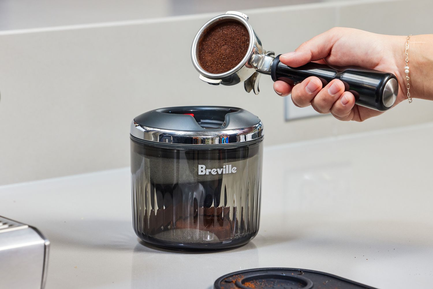 A person about to place a portafilter with espresso grounds in it into the Breville Puck Sucker.