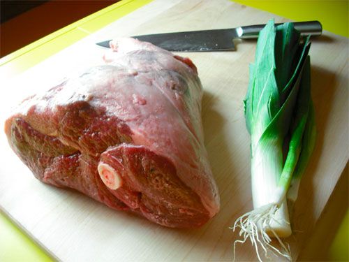A large leg of raw lamb next to a leek for making Hunan lamb