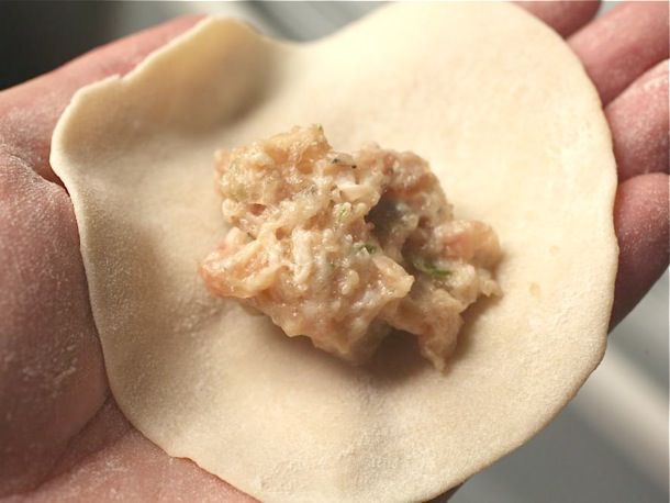 A homemade dumpling wrapper in an open palm topped with a spoonful of filling.