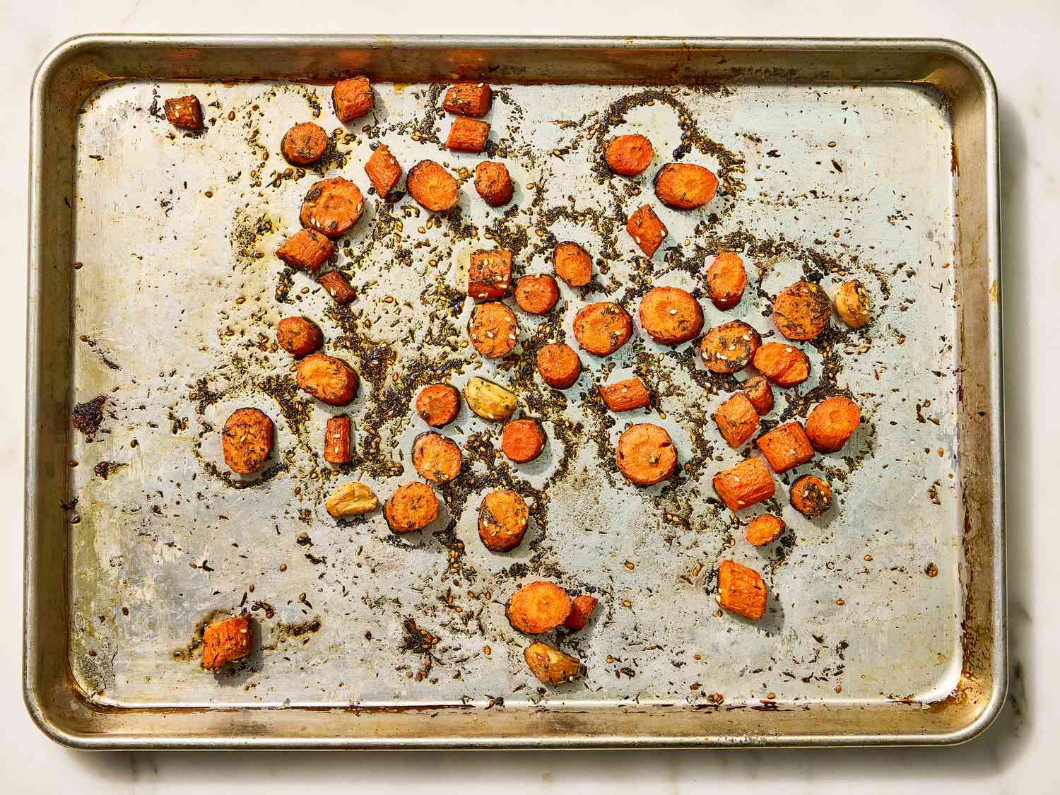 A baking sheet with roasted carrot slices and herbs